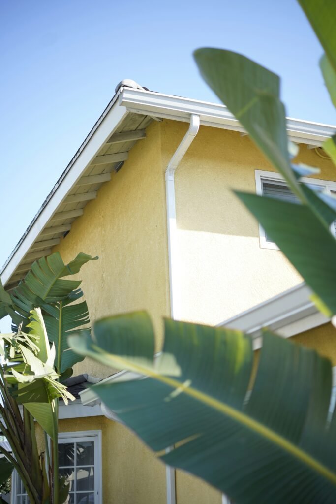 Freshly cleaned white gutters on a yellow Florida home surrounded by tropical plants, after professional gutter cleaning by Suncoast Softwash in Brevard County.